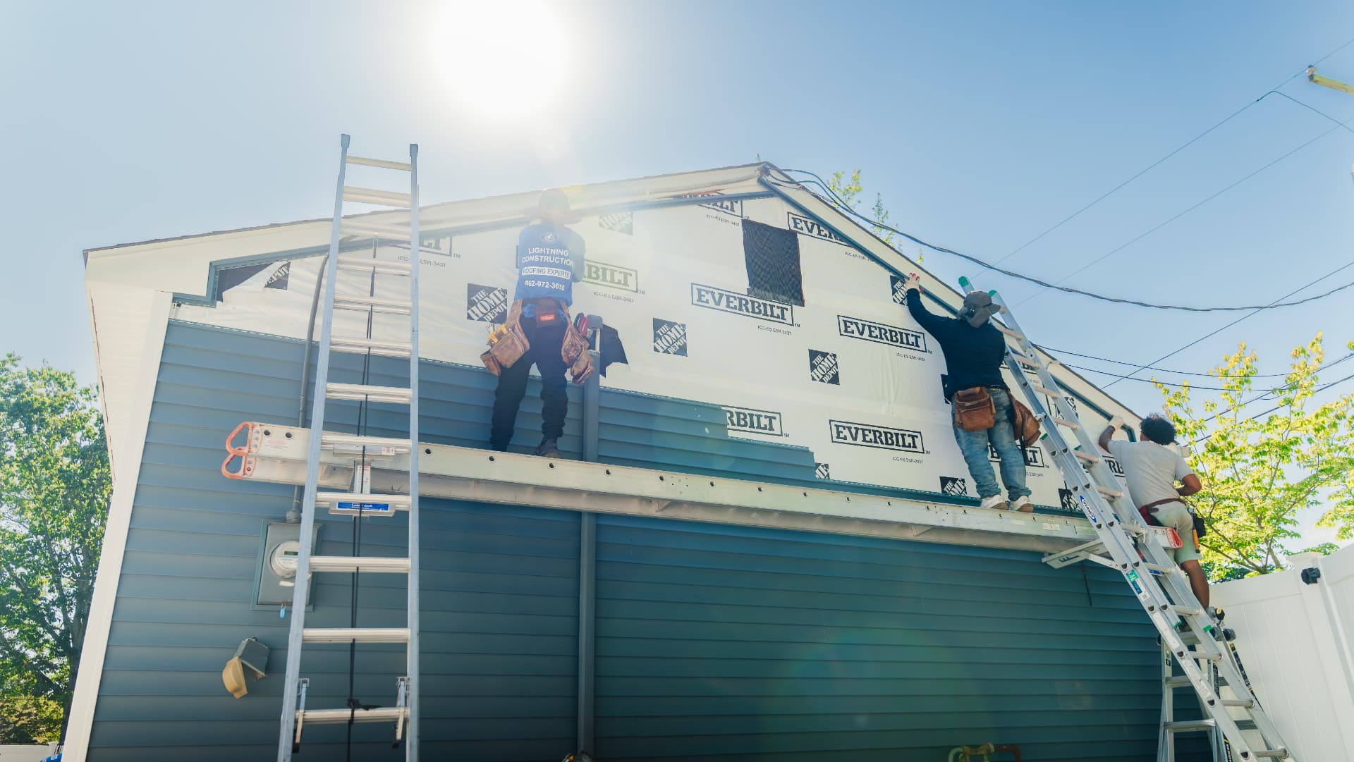 Roofing crew working on a gable wrapped in house wrap under bright sun