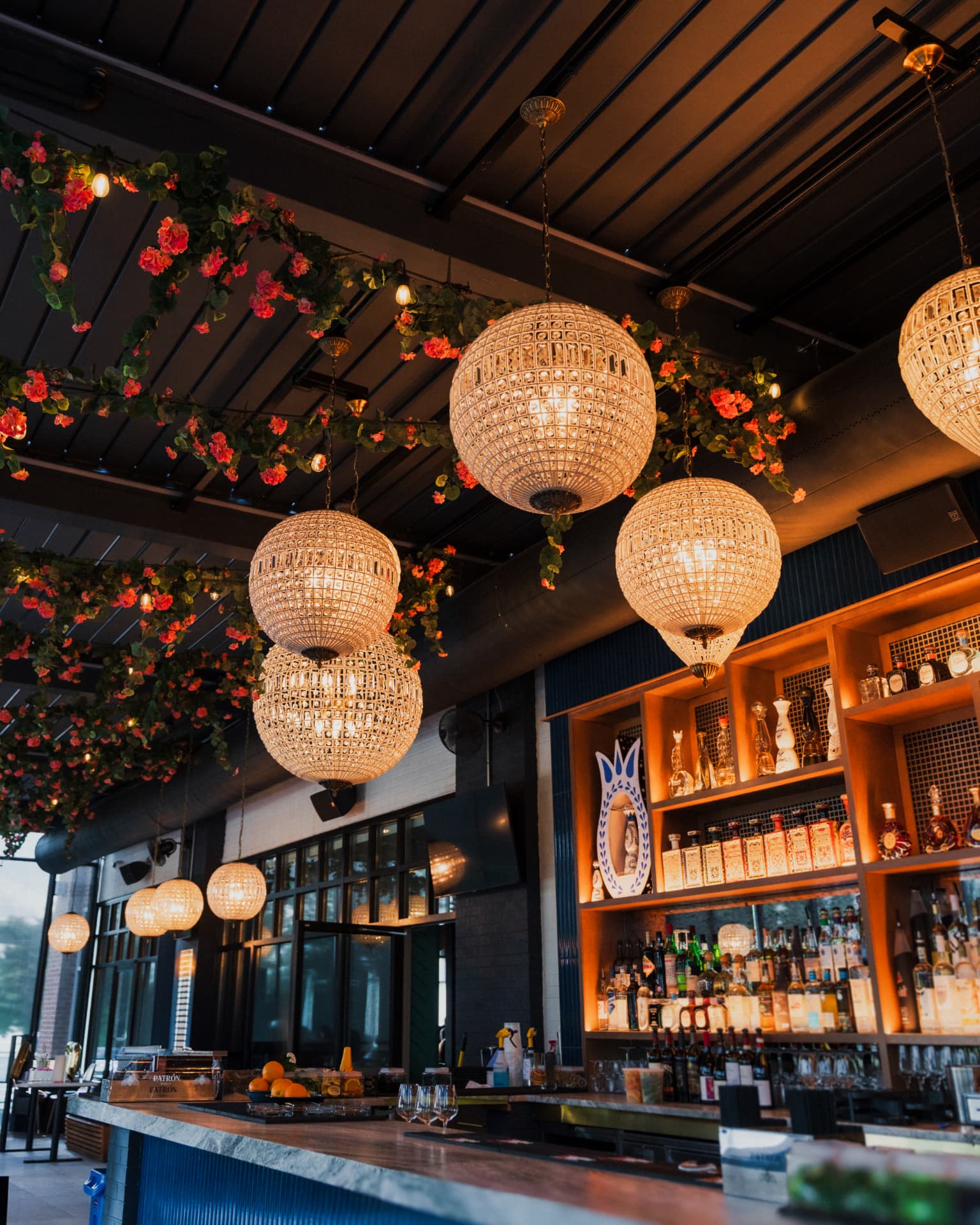 Chandelier-lit restaurant bar interior with trailing greenery and backlit shelves