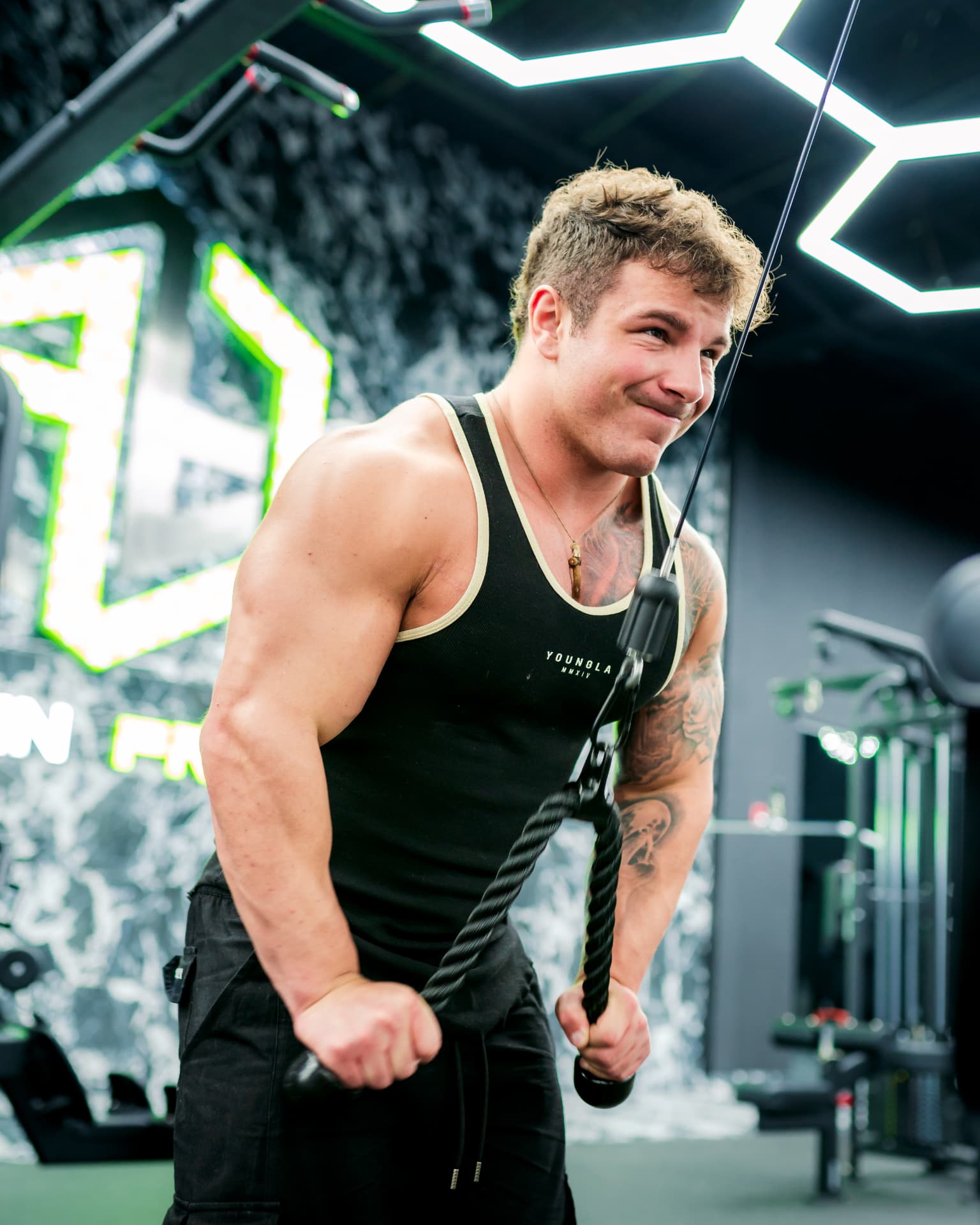 Athlete performing triceps pushdowns on a cable machine in a gym wearing a Youngla tank top