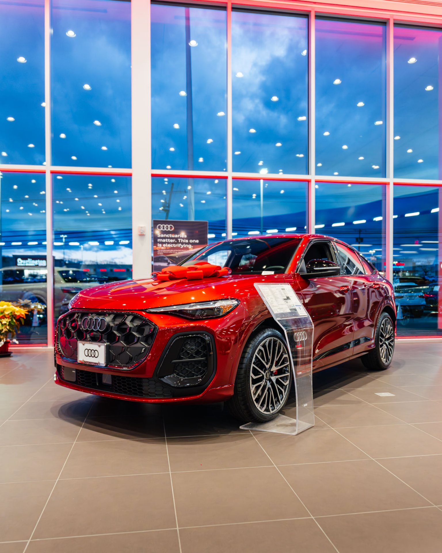 Red Audi SUV with a gift bow in a dealership showroom at dusk