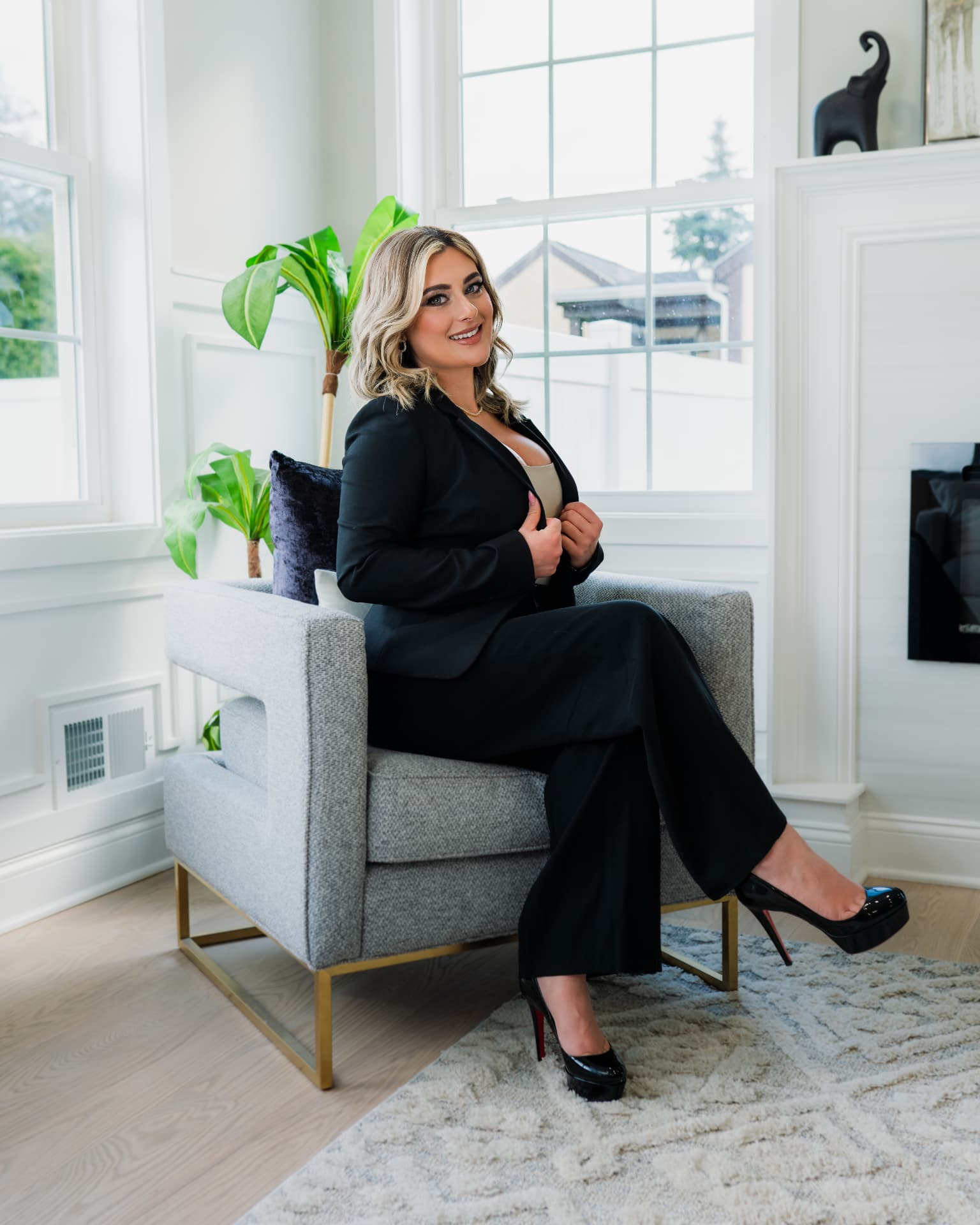 Woman in a black professional suit sitting in a modern grey armchair in a bright studio room