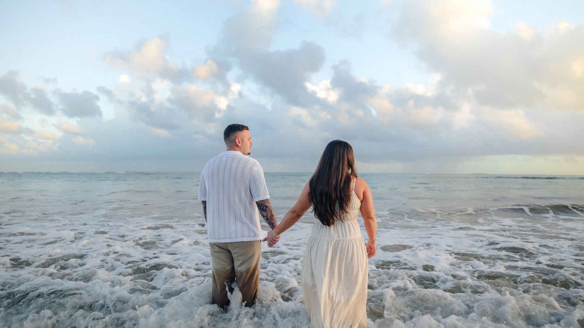 Couple holding hands in the ocean surf at sunrise